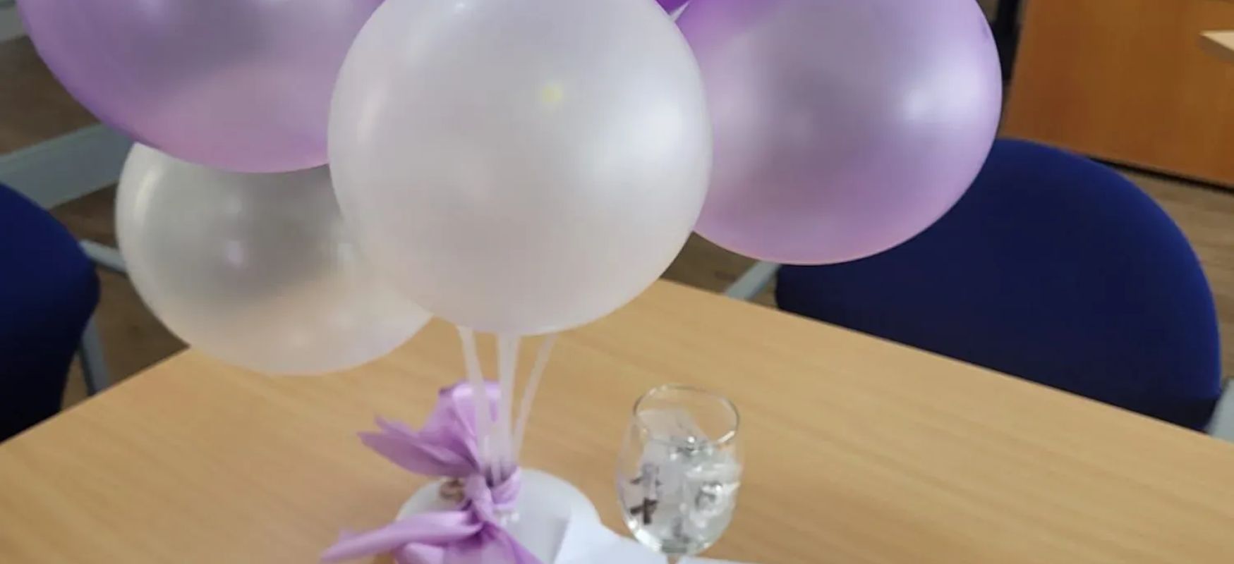 Luftballons in weissen und violetten farben stehen auf einem tisch mit einem weinglas und einem zettel im buero