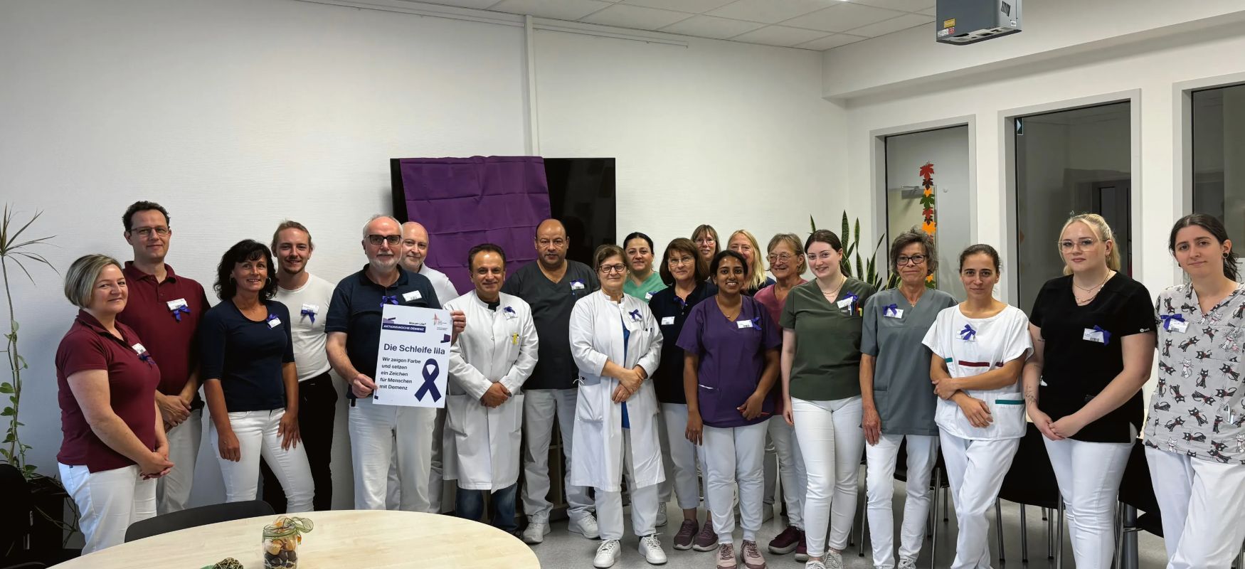 Gruppe von medizinischen mitarbeitern steht in einem raum einige tragen weiße kittel und halten ein schild mit lila schleife